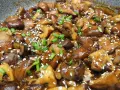 Champignons caramélisés chinois, brillants et appétissants, saupoudrés de graines de sésame et de ciboule fraîche.