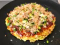 Un délicieux okonomiyaki, un plat emblématique du repas japonais maison, garni d'oignons verts et de flocons de bonite.