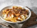 Une assiette de poutine fumante, parfaite pour une recette poutine maison facile. Des frites croustillantes, du fromage en grains et une sauce brune onctueuse.