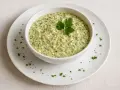 Un bol de sauce gribiche crémeuse, parsemée de persil frais et de petits morceaux d'œuf dur, garni d'une feuille de persil.
