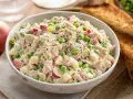 Salade de thon crémeuse avec des morceaux de pomme rouge, des petits pois et du céleri, garnie d'herbes fraîches et de poivre noir.