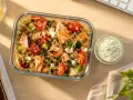 Salade de quinoa avec saumon grillé, tomates, concombre et feta, parfaite pour un repas lunch sain. Sauce crémeuse à l'aneth à côté.