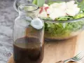 Bouteille de sauce salade facile, prête à être versée sur une salade fraîche et croquante dans un bol en verre.