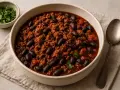 Un bol de chili con carne, une recette réconfortante avec viande hachée et haricots noirs, garni de persil frais.