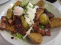 Une généreuse salade vosgienne avec des pommes de terre, lardons, œuf poché et croûtons sur un lit de verdure.
