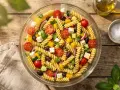 Salade de pâtes colorée avec tomates cerises, concombre, olives, poivrons jaunes et feta. Un plat frais et estival.