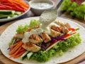 Sauce crémeuse versée sur un wrap garni de poulet grillé, laitue, carottes, concombre et chou rouge. Parfait pour une recette sauce wrap facile.