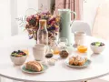Un délicieux déjeuner vegan avec fruits frais, pain artisanal, granola et jus d'orange, présenté sur une table blanche.