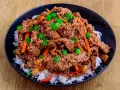 Un bol de riz blanc garni de boeuf bulgogi mariné, de julienne de carottes et d'oignons verts ciselés, parsemé de graines de sésame.