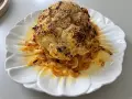 Un chou-fleur entier, rôti au four, est servi sur une assiette blanche ornée d'oignons caramélisés. Le chou-fleur est saupoudré de graines de sésame et d'épices.