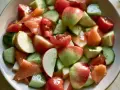 Salade fraîche et colorée : morceaux de concombre, tomates cerises, pommes rouges et saumon fumé, le tout servi dans un bol.