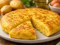 Une délicieuse tortilla espagnole, avec une part coupée, prête à être dégustée. Des pommes de terre et des oignons sont visibles en arrière-plan.