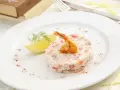 Délicieux tartare de crevette thaï, garni d'une crevette grillée et d'une tranche de citron, sur une assiette blanche.