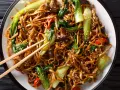 Un plat de chow mein appétissant avec des nouilles, des légumes verts croquants, des champignons et des poivrons rouges, saupoudré de graines de sésame.
