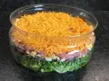 Salade à étage colorée dans un bol en verre : laitue, petits pois, oignons rouges, jambon, œufs durs et fromage râpé.
