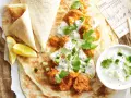 Un plat de butter chicken crémeux servi sur du pain naan avec du raïta et des quartiers de citron.