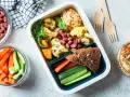 Un repas tiré du sac sain et coloré : houmous, légumes rôtis, haricots rouges, pain complet et crudités. Parfait pour un déjeuner sur le pouce.