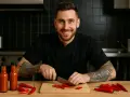 Chef souriant prépare une sauce piquante recette facile. Des piments rouges et des bouteilles de sauce sont sur la table.