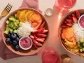 Deux bols colorés remplis de riz, fraises, myrtilles, concombre, carottes et oranges. Une belle idée poke bowl pour un repas frais et sain.