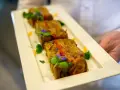 Trois tranches de terrine de légumes, garnies de fleurs comestibles et de verdure, présentées sur une assiette blanche par un serveur.