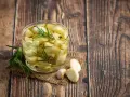 Un bocal de **ail confit** avec des brins de romarin et quelques grains de poivre, posé sur une toile de jute, sur un fond de bois rustique.
