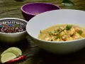 Un plat de crevette curry coco crémeux, garni de coriandre fraîche, servi avec des quartiers de citron vert et un piment rouge.