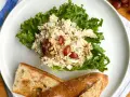 Salade de poulet froid mayonnaise sur laitue, avec des raisins et des noix, servie avec du pain croustillant.
