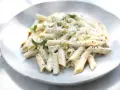 Pâtes penne nappées d'une sauce crémeuse à l'ail, parsemées de fines herbes fraîches, servies sur une assiette blanche.