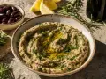 Un bol de caviar d'aubergine crémeux, garni d'herbes fraîches et d'huile d'olive, avec des olives, des quartiers de citron et du romarin en arrière-plan.