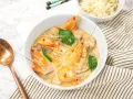 Un plat de sauté crevettes thaï lait de coco, garni de feuilles vertes, servi avec du riz et une cuillère en cuivre.