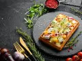 Gaufre salée garnie de fromage, de dés de mangue et de pousses vertes, sur une ardoise noire.