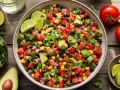 Salade mexicaine recette : un plat coloré avec haricots noirs, maïs, avocat, tomates, oignons rouges et jalapeños, garni de coriandre et de quartiers de citron vert.