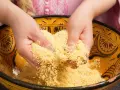 Mains travaillant du couscous marocain dans un plat traditionnel décoré.