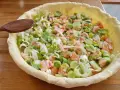 Préparation d'un plat végétarien : une tarte garnie de saumon et de poireaux coupés, prête à être cuite.