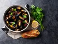 Un plat de moules au rosé, garni de persil frais, avec un quartier de citron et une baguette à l'ail.