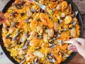 Un plat généreux de poulet paella, garni de crevettes et de moules, prêt à être dégusté par plusieurs mains.