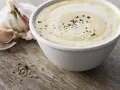 Sauce césar sans oeuf crémeuse, parsemée de poivre noir, avec une tête d'ail en arrière-plan sur fond de bois.