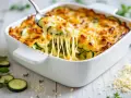 Une cuillère soulève une portion généreuse de gratin de légumes, révélant des courgettes fondantes sous un fromage doré et filant.