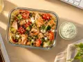 Un délicieux repas chaud à emporter pour le midi : quinoa, saumon grillé, tomates, concombre et feta, avec une sauce crémeuse. Parfait pour un déjeuner sain au bureau.