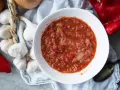 Un bol de salsa facile, avec des tomates, des oignons et des poivrons rouges. Des gousses d'ail et un oignon sont disposés autour.