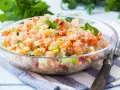 Salade quinoa colorée avec des dés de tomates, carottes, concombre et maïs, garnie de feuilles de menthe fraîche.