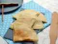 Pile de crêpes dorées, prêtes à être garnies. La pâte à crêpe vegan est légère et aérienne. Un ustensile en bois est à côté.
