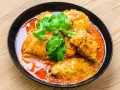 Un plat de poulet vindaloo, un curry indien épicé, servi dans un bol noir avec de la coriandre fraîche.