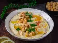 Un plat de houmous crémeux, garni de pois chiches, persil et paprika. Parfait pour découvrir 7 recettes de houmous maison.