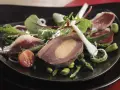 Une délicieuse salade landaise avec du foie gras, du magret de canard, des asperges et des tomates cerises sur une assiette noire.