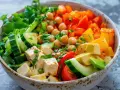 Un bol coloré de salade originale avec tofu, pois chiches, concombre, poivrons, avocat et herbes fraîches.