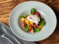 Salade colorée avec œuf poché, tomates cerises, lardons et quelques feuilles de salade légumes verts.