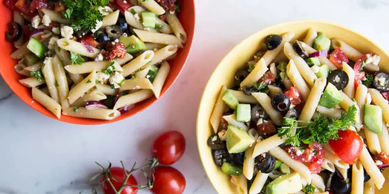 Deux bols de salade de pâtes méditerranéenne colorée, garnie de feta, olives, tomates et avocat.