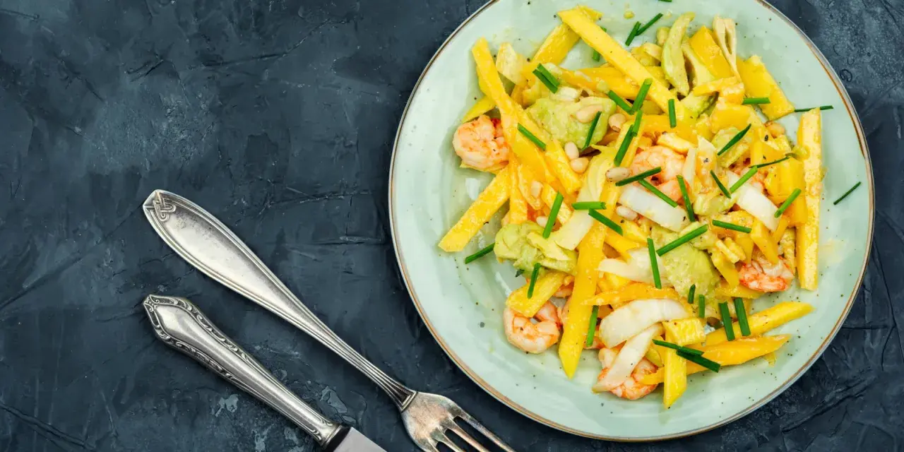 Salade colorée avec des crevettes, de l'avocat et des bâtonnets de mangue, garnie de ciboule. Un délice frais et fruité.