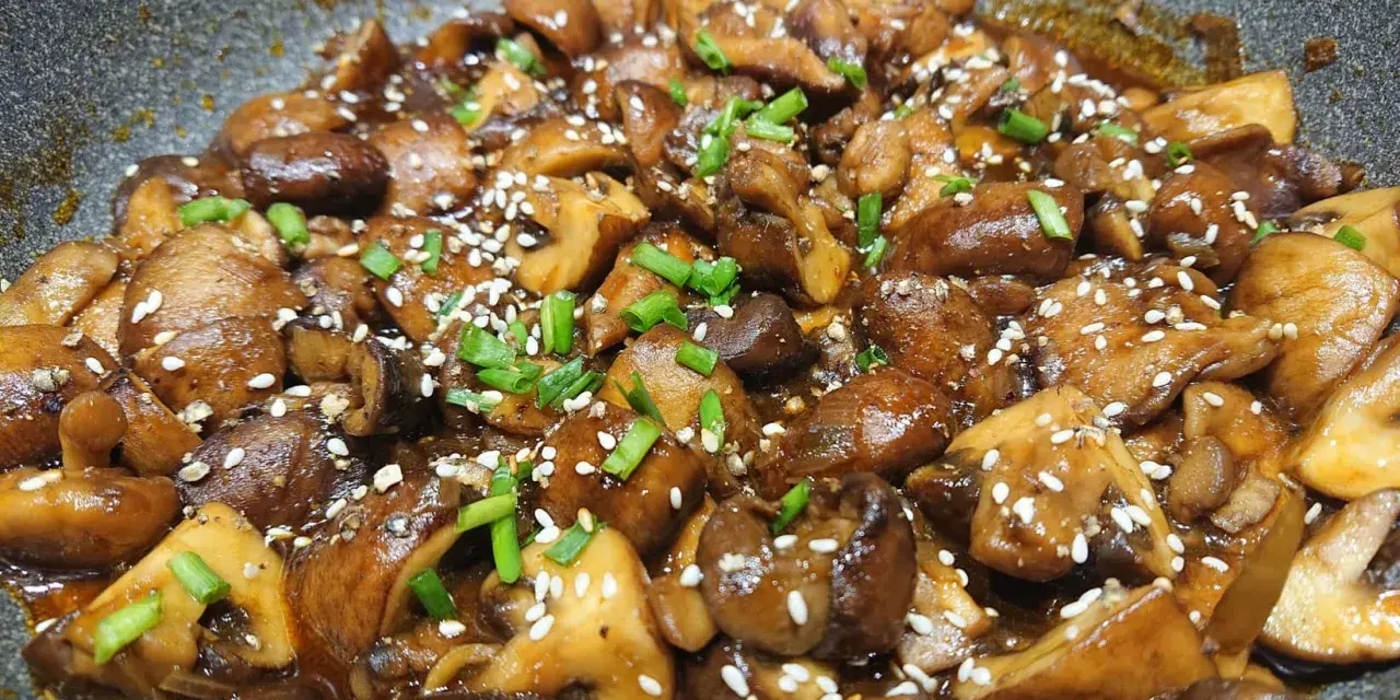 Champignons caramélisés chinois, brillants et appétissants, saupoudrés de graines de sésame et de ciboule fraîche.